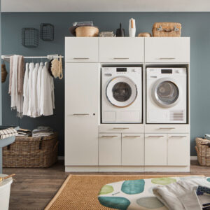 Ein Waschraum mit Waschmaschine und Trockner im weißen Möbelmodul, Kleiderstange mit Hemden, Körben und einem Wandwaschtrog.