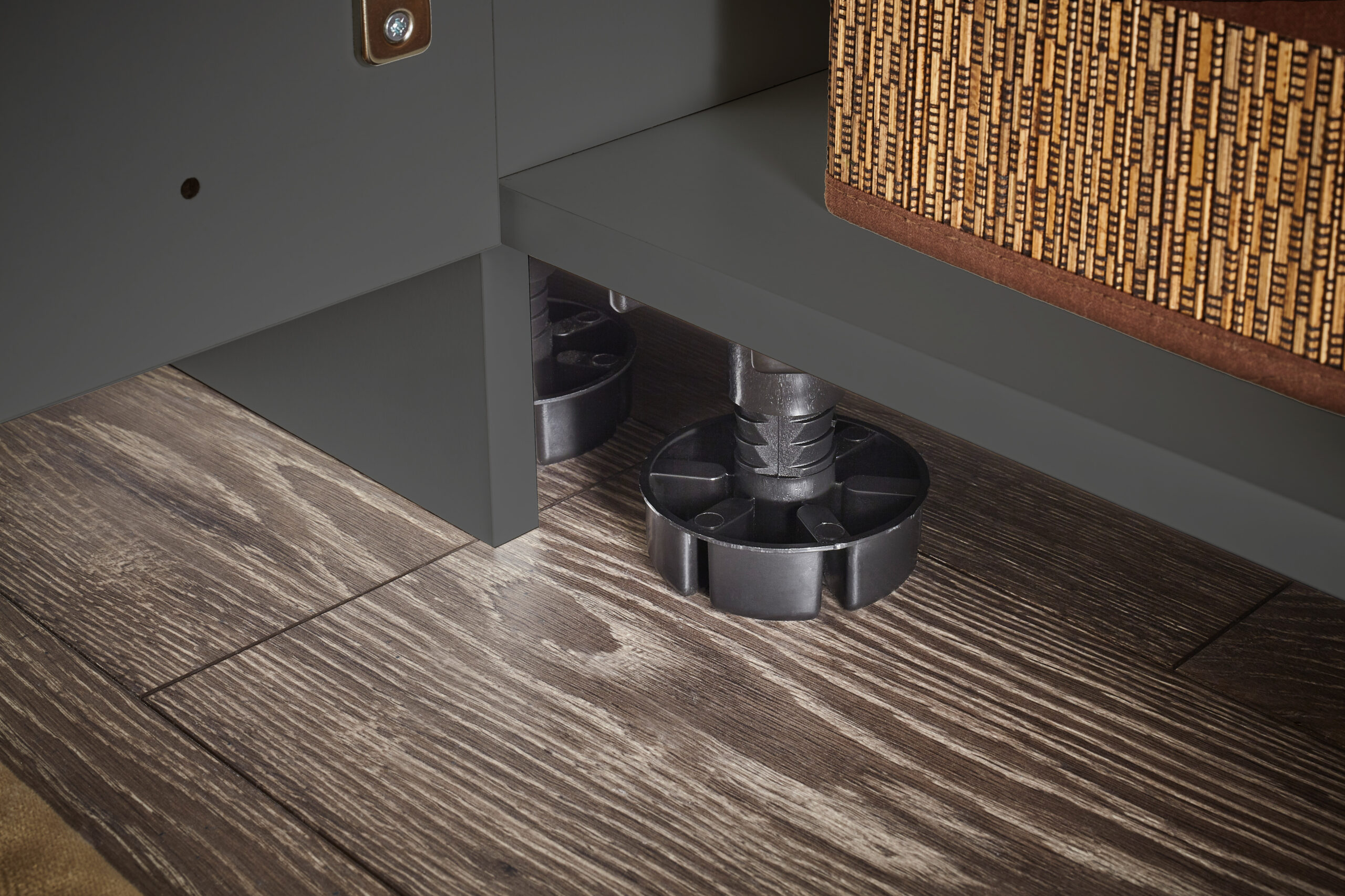 Detailaufnahme von höhenverstellbarem Möbelfuß unter einem Schrank auf Holzfußboden.