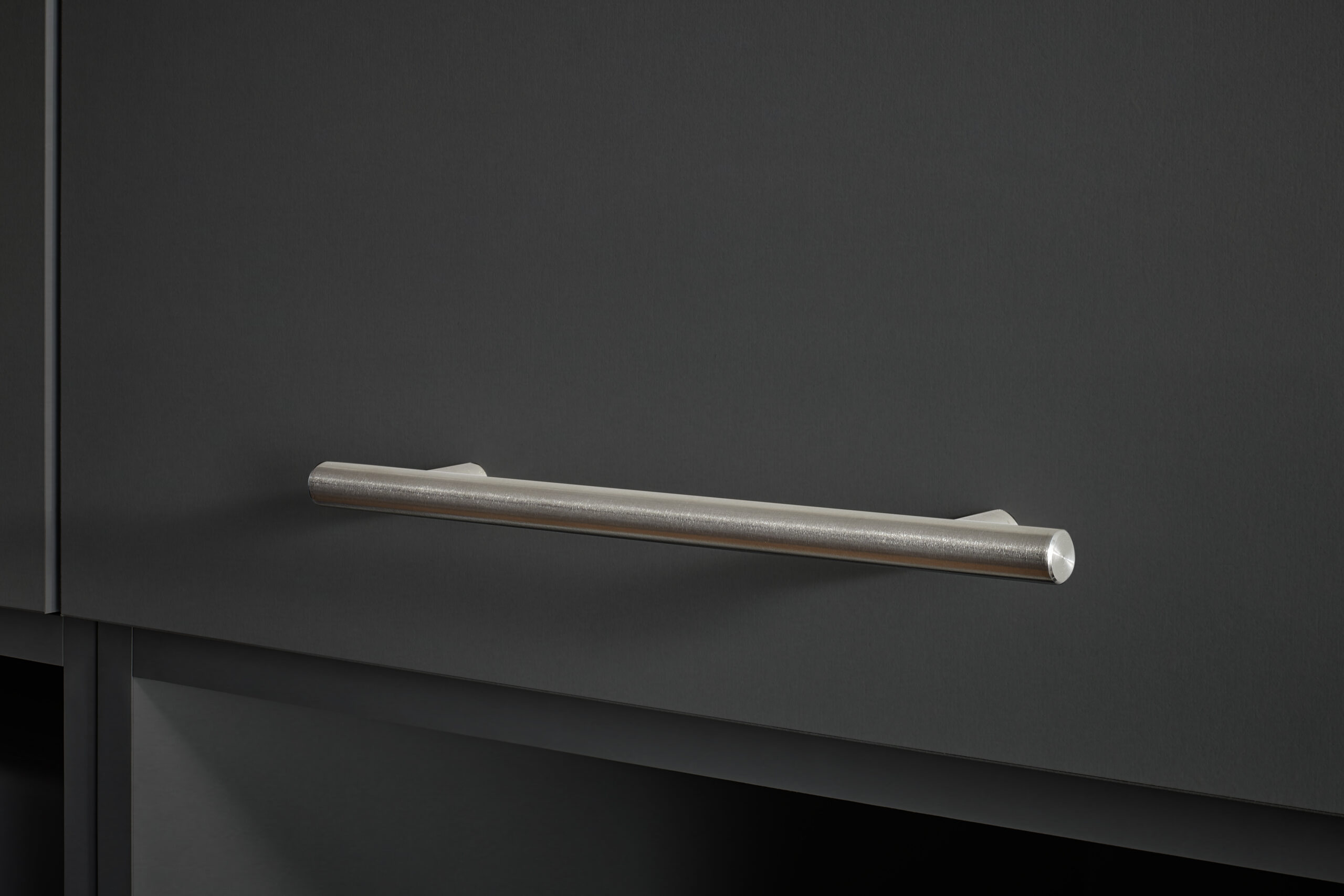 Detailaufnahme eines horizontalen Metallgriffs an einer dunklen Schrankfront.