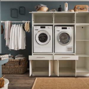 Geöffnete weiße Waschkombination mit Waschmaschine, Trockner und vielen offenen Fächern in einem Hauswirtschaftsraum.