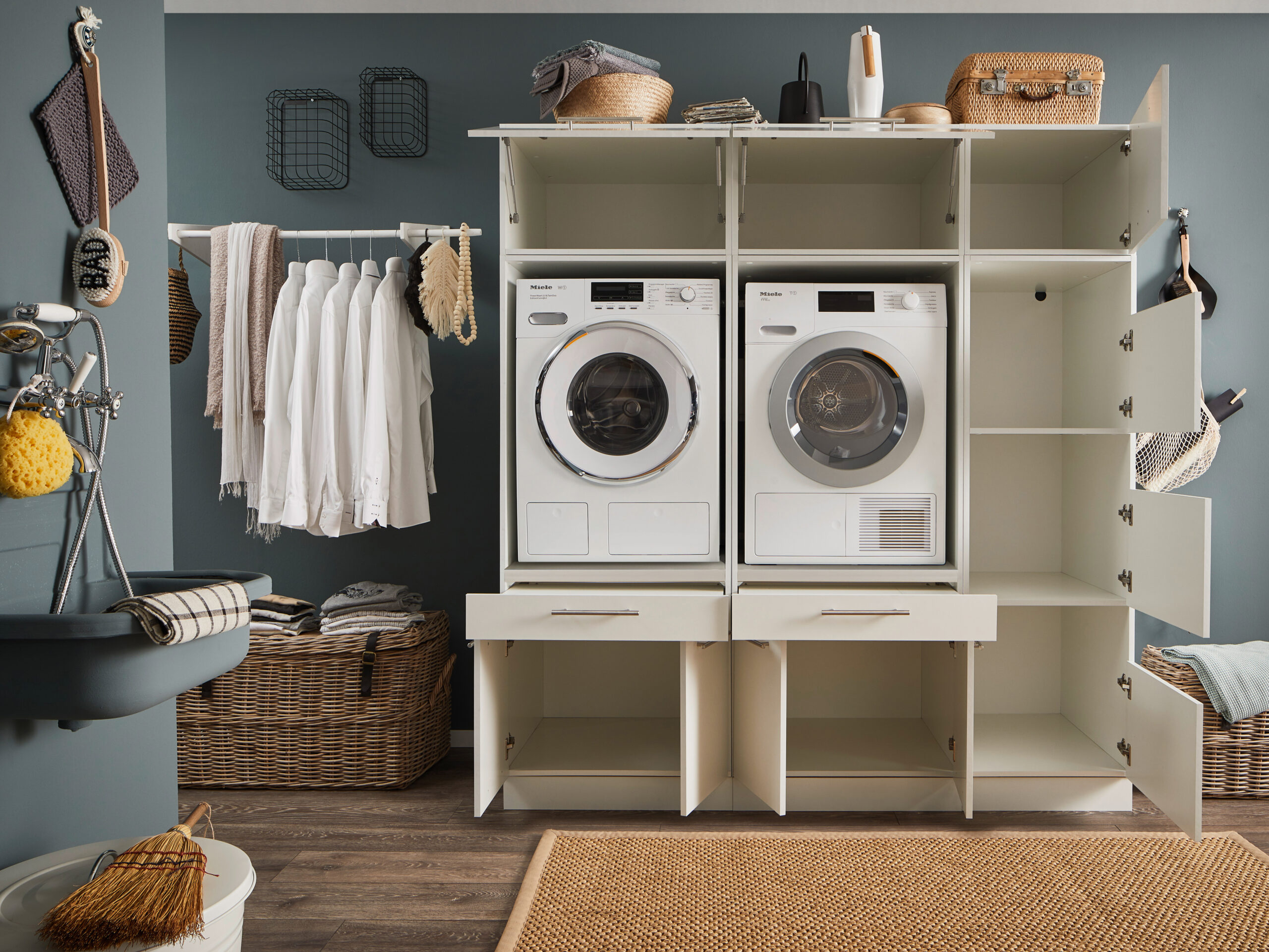 Geöffnete weiße Waschkombination mit Waschmaschine, Trockner und vielen offenen Fächern in einem Hauswirtschaftsraum.