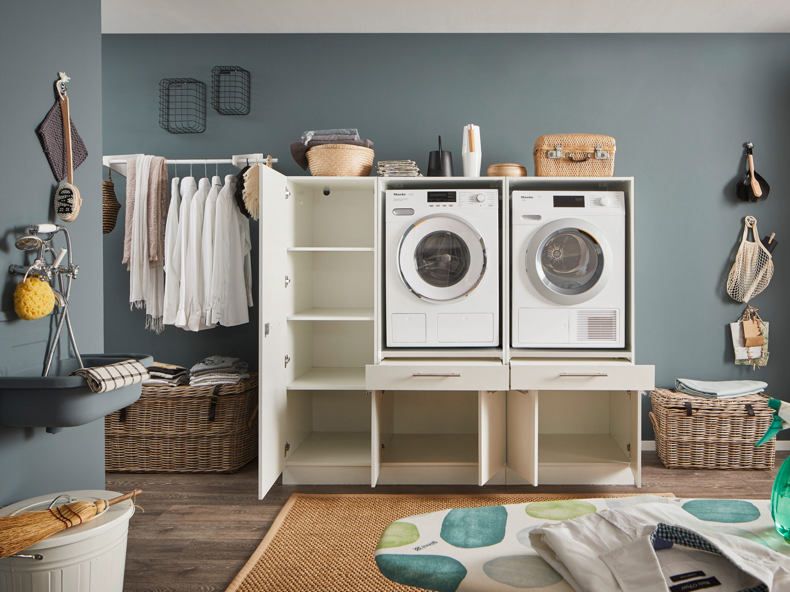 Weißer Waschmaschinen und Trockner Schrank mit geöffnetem Seitenschrank und offenen unteren Fächern in modernem Hauswirtschaftsraum.