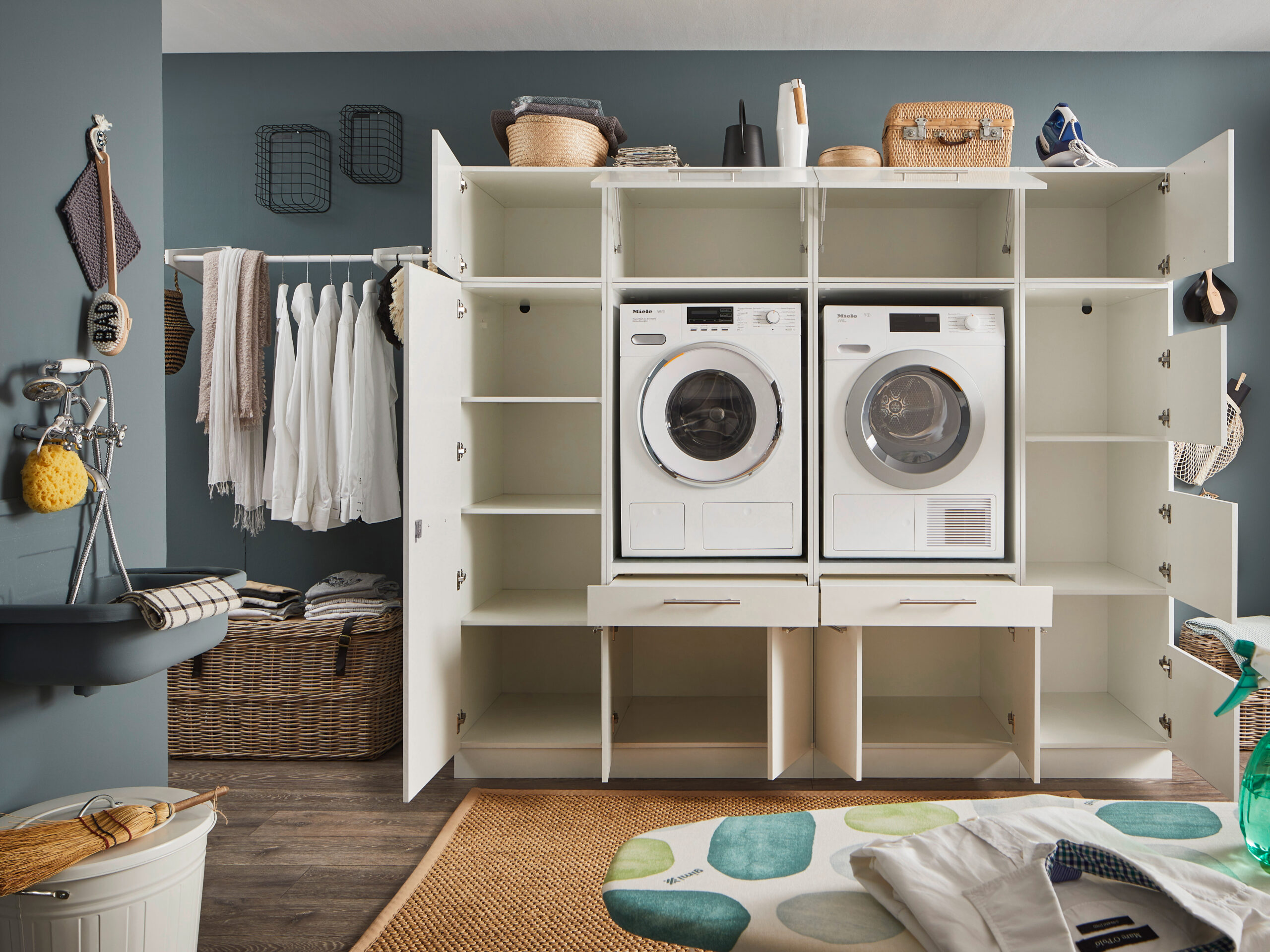 Waschraum Schrankwand in Weiß mit geöffneten Türen, sichtbaren Innenfächern, zwei integrierten Geräten und umliegender moderner Waschküche.