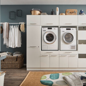 Ein großer Waschraum mit Waschmaschine und Trockner im weißen Möbelmodul, offenen Stauraumfächern, Körben, einer Kleiderstange und einem Waschtrog.