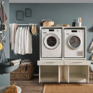 Weiße Doppelstation für Waschmaschine und Trockner in einem Haushaltsraum mit geöffneten unteren Fächern.