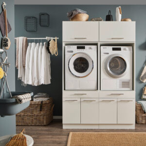 Ein moderner Waschraum mit Waschmaschine und Trockner in einem weißen Möbelmodul, Kleiderstange mit weißen Hemden, Körben und einem Wandwaschtrog.