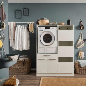 Ein Waschraum mit eingebauter Waschmaschine, offenen Stauraumfächern, Kleiderstange mit weißen Hemden, Körben und einem Wandwaschtrog.