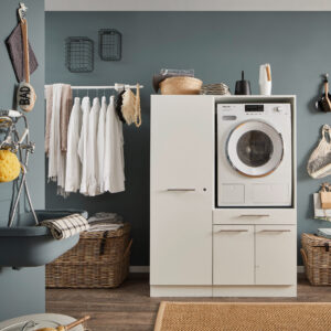 Waschbereich mit Schrankmodul Ein moderner Waschraum mit eingebauter Waschmaschine im weißen Möbelmodul, Kleiderstange mit Hemden, Körben und einem Wandwaschtrog.